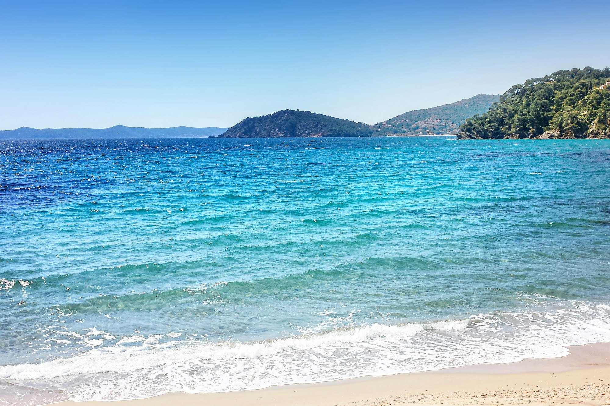 Une plage de sable et l’eau turquoise au pied des collines