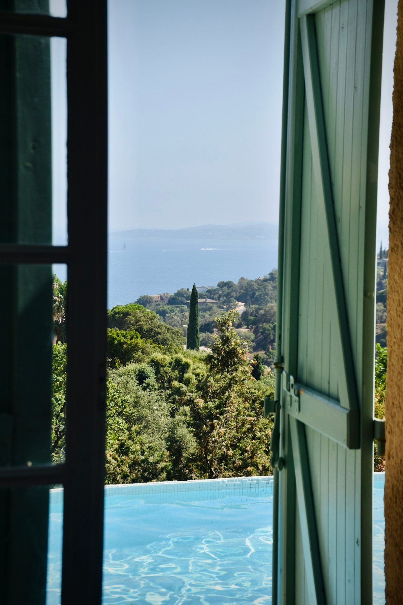 Volets verts ouverts sur la piscine, les cyprès et la mer